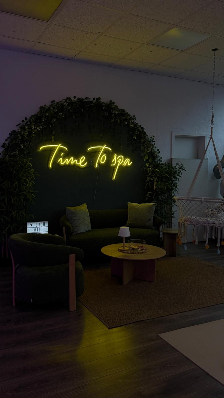 Sofa und Neonschriftzug Time To spa vor der Blätterwand